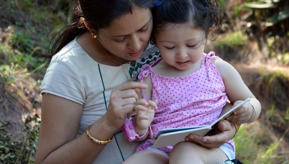 Livelihood Parenting -Honey Maheshwari Phonics the Method Explained Step by Step - Livelihood Parenting by Honey Maheshwari Mother and daughter sitting outdoors, reading a small book together on a sunny day.